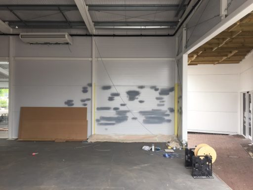 Kingspan Cladding: before respray Interior of a space with a partially painted wall, debris, and tools scattered on the floor.